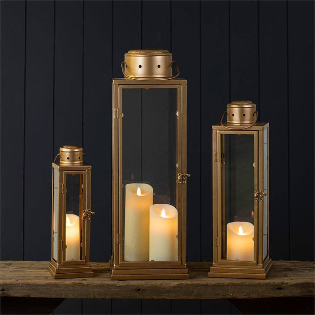 Set of gold lanterns with candles on a wooden surface against a dark wooden panel background