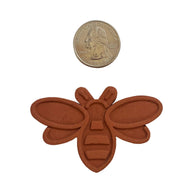 Brown bee-shaped object next to a coin on a white background