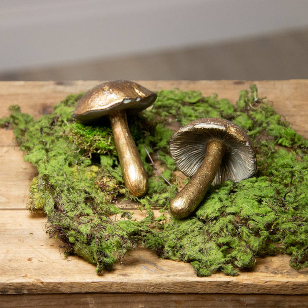 Two metallic mushrooms on a bed of green moss on a wooden surface.