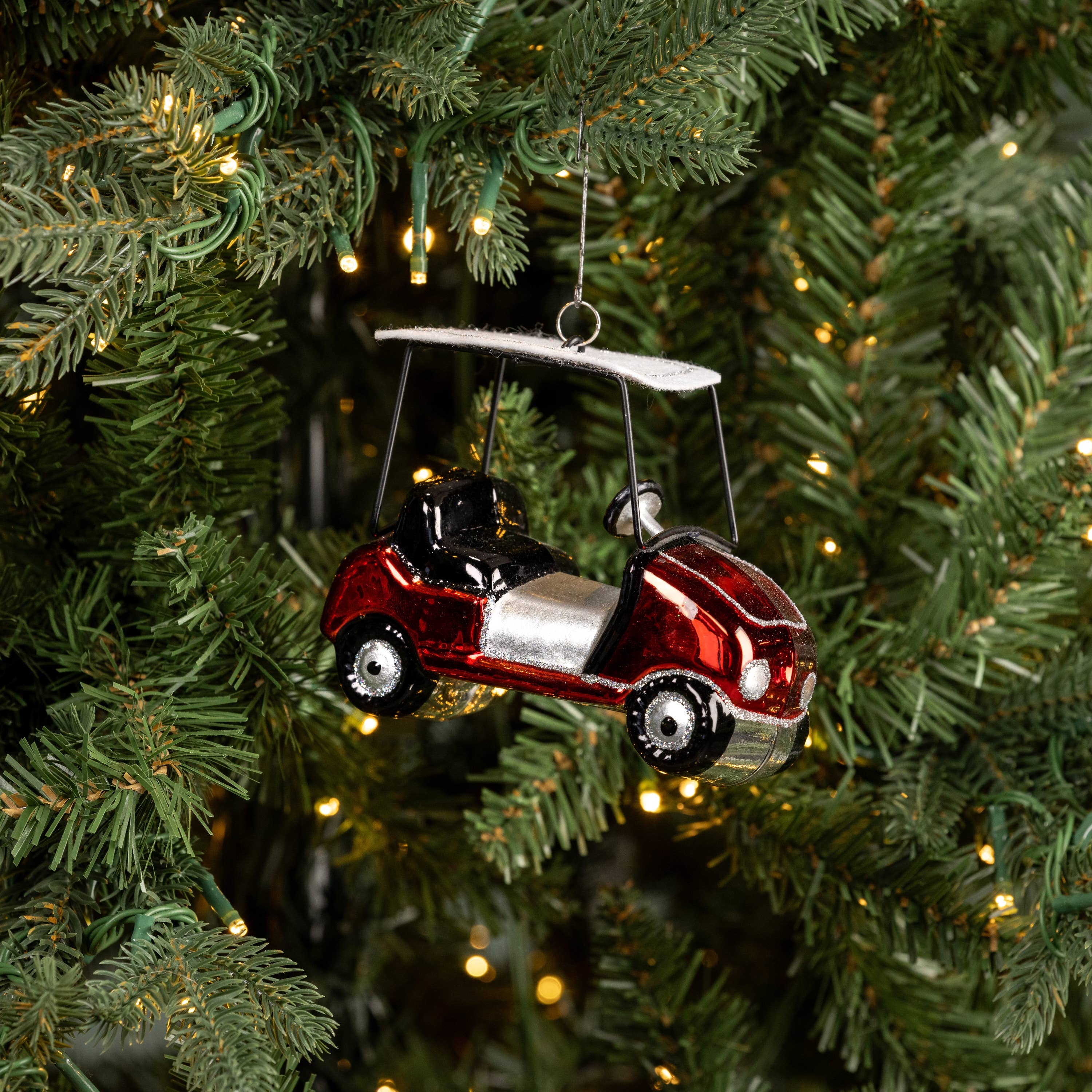 Decorative ornament of a red car with a canopy hanging on a Christmas tree.