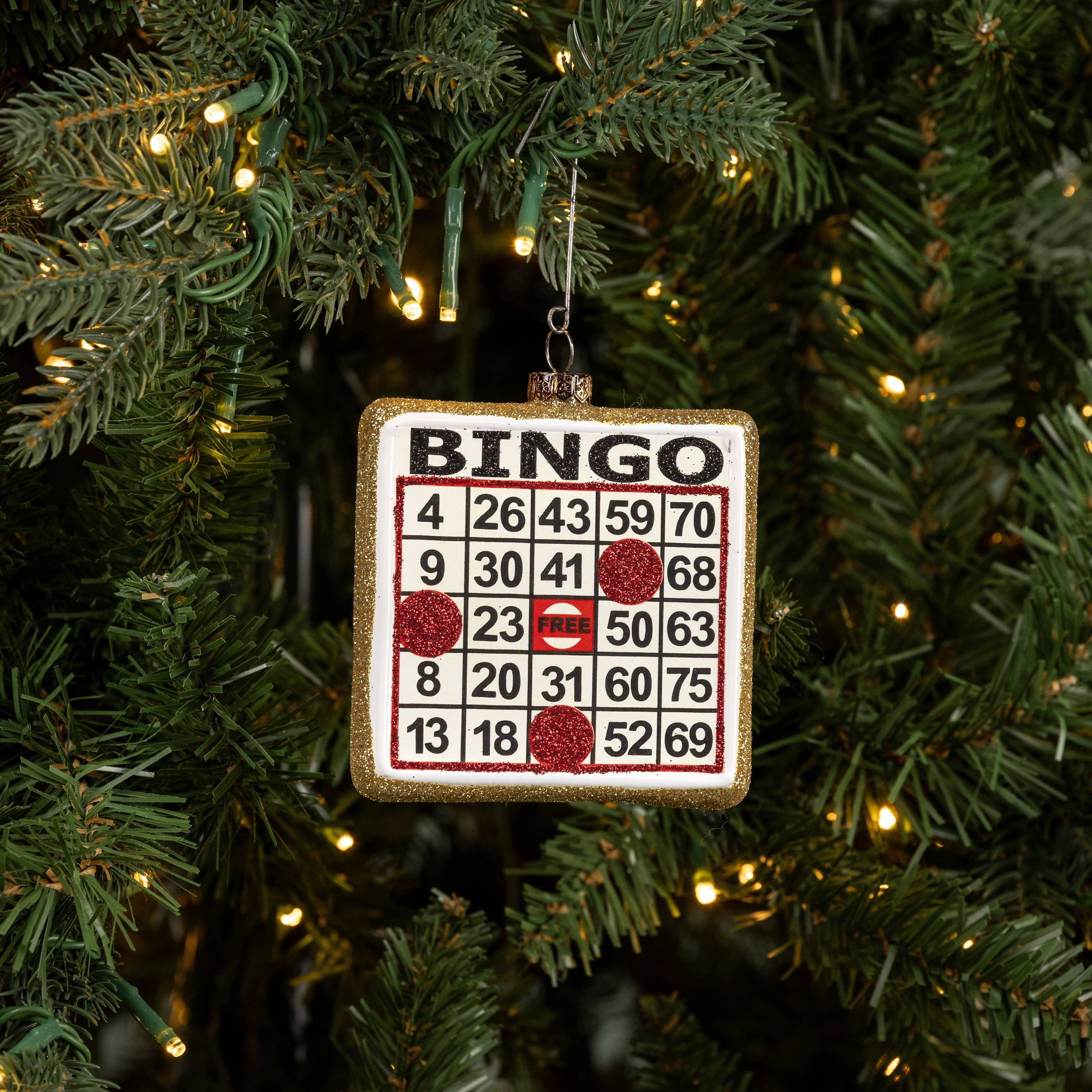 Bingo card ornament hanging on a Christmas tree with lights.