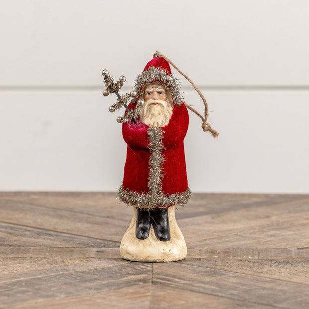 Decorative figure of a Santa Claus holding a bundle of sticks on a wooden surface.