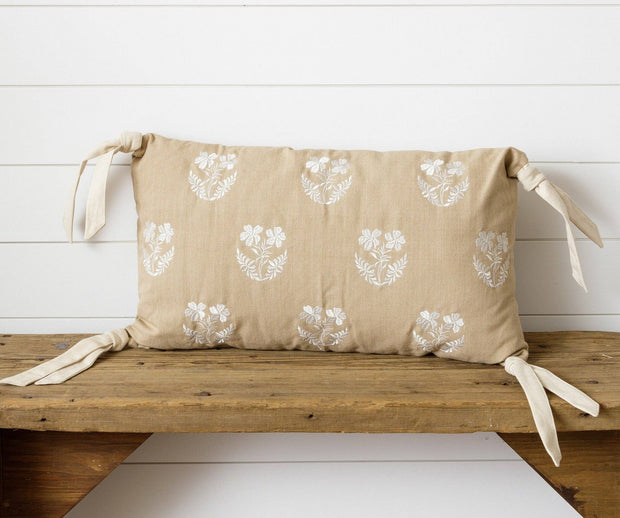 Beige cushion with white floral patterns on a wooden bench against a white wooden panel background