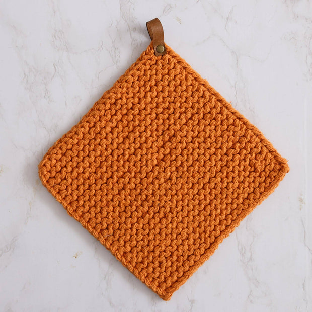 Knitted orange pot holder with a leather strap on a white marble background