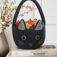 Black cat-shaped basket with colorful treats on top of books, against a white wall.