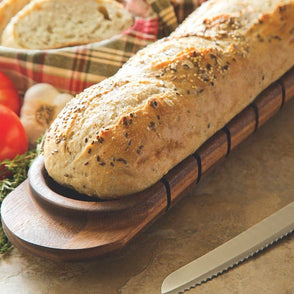 Loaf of bread on a wooden board with tomatoes and herbs on a checkered cloth.