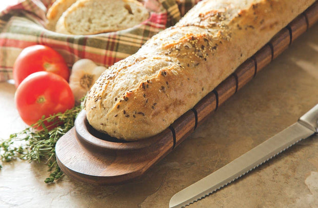 Loaf of bread on a wooden board with tomatoes and herbs on a checkered cloth.