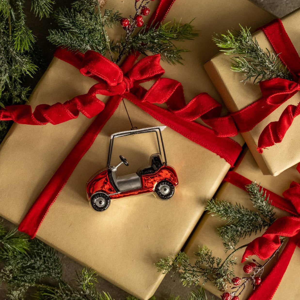 Gift wrapped in brown paper with a red ribbon, surrounded by greenery and a small red golf cart ornament.