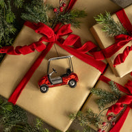 Gift wrapped in brown paper with a red ribbon, surrounded by greenery and a small red golf cart ornament.