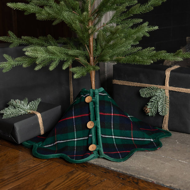 Christmas tree with a plaid skirt and presents underneath on a wooden floor.