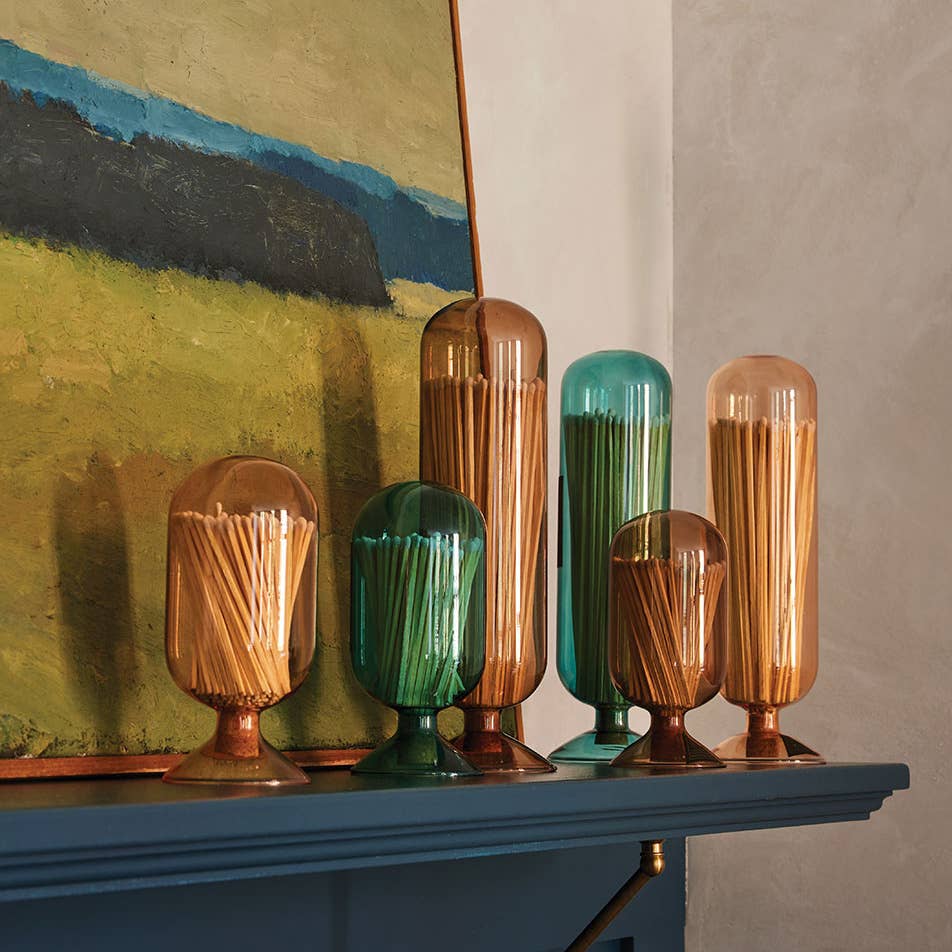 Set of colorful glass containers on a shelf with a painting in the background