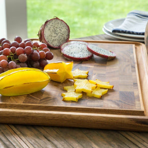 Wooden cutting board with sliced yellow fruit and red grapes on a wooden table.