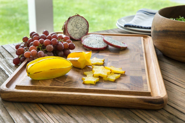 Wooden cutting board with sliced yellow fruit and red grapes on a wooden table.