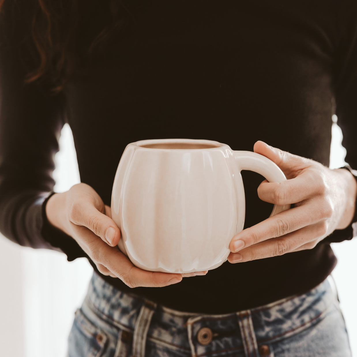 Person holding a white ceramic mug with a blurred background