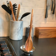 Wooden spoon in a metal holder on a kitchen counter with a marble utensil holder in the background.