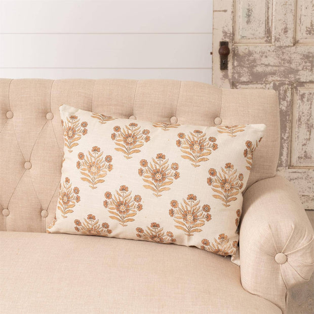 Decorative pillow with floral pattern on a beige sofa against a rustic wooden wall.