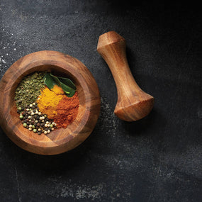 Wooden mortar and pestle with assorted spices on a dark surface