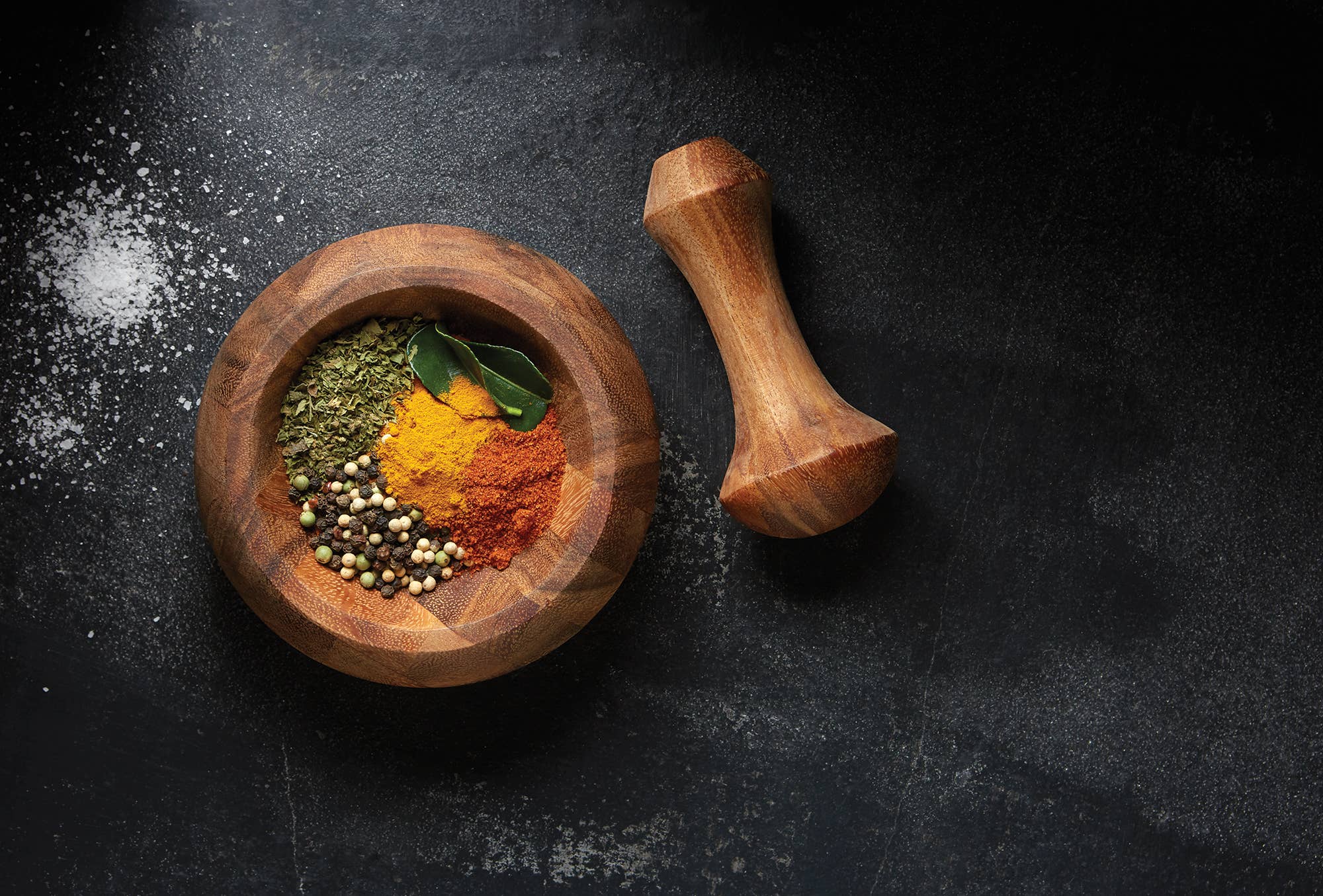 Wooden mortar and pestle with assorted spices on a dark surface