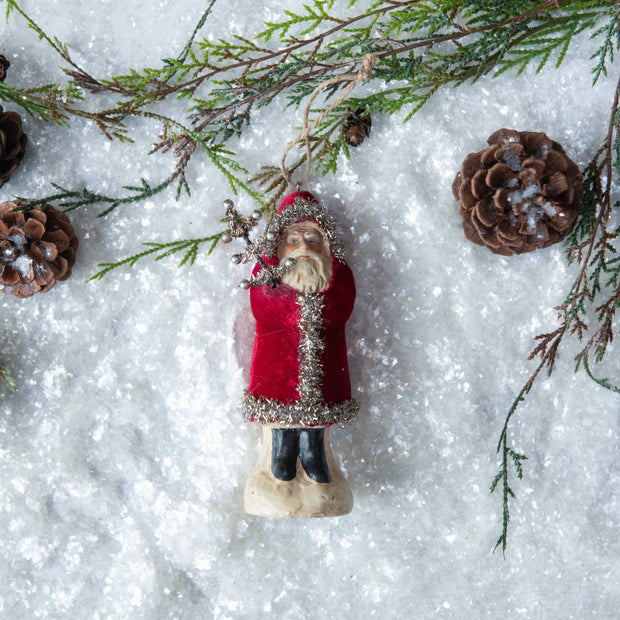 Decorative figure of a person in a red coat with pinecones and branches on a snowy background