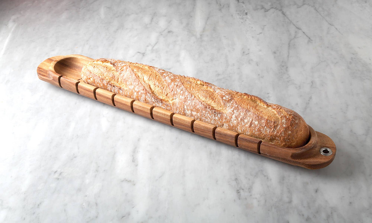 Long loaf of bread in a wooden bread holder on a light gray surface