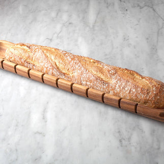 Long loaf of bread in a wooden bread holder on a light gray surface