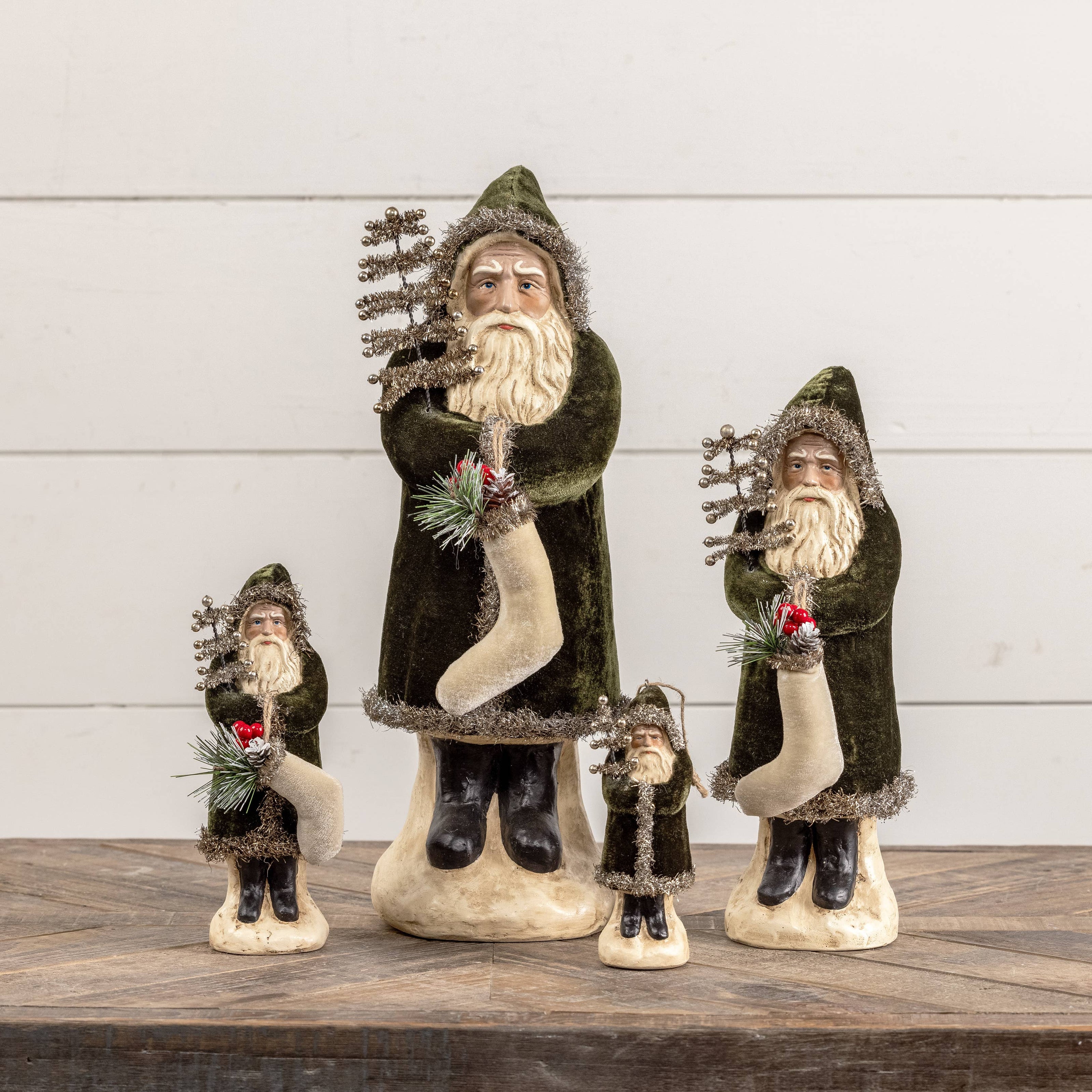 Set of four decorative Santa Claus figures on a wooden surface with a white wooden panel background.
