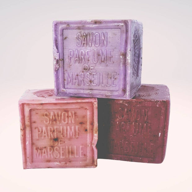 Three bars of Savon Parfumé de Marseille soap in different colors on a white background.