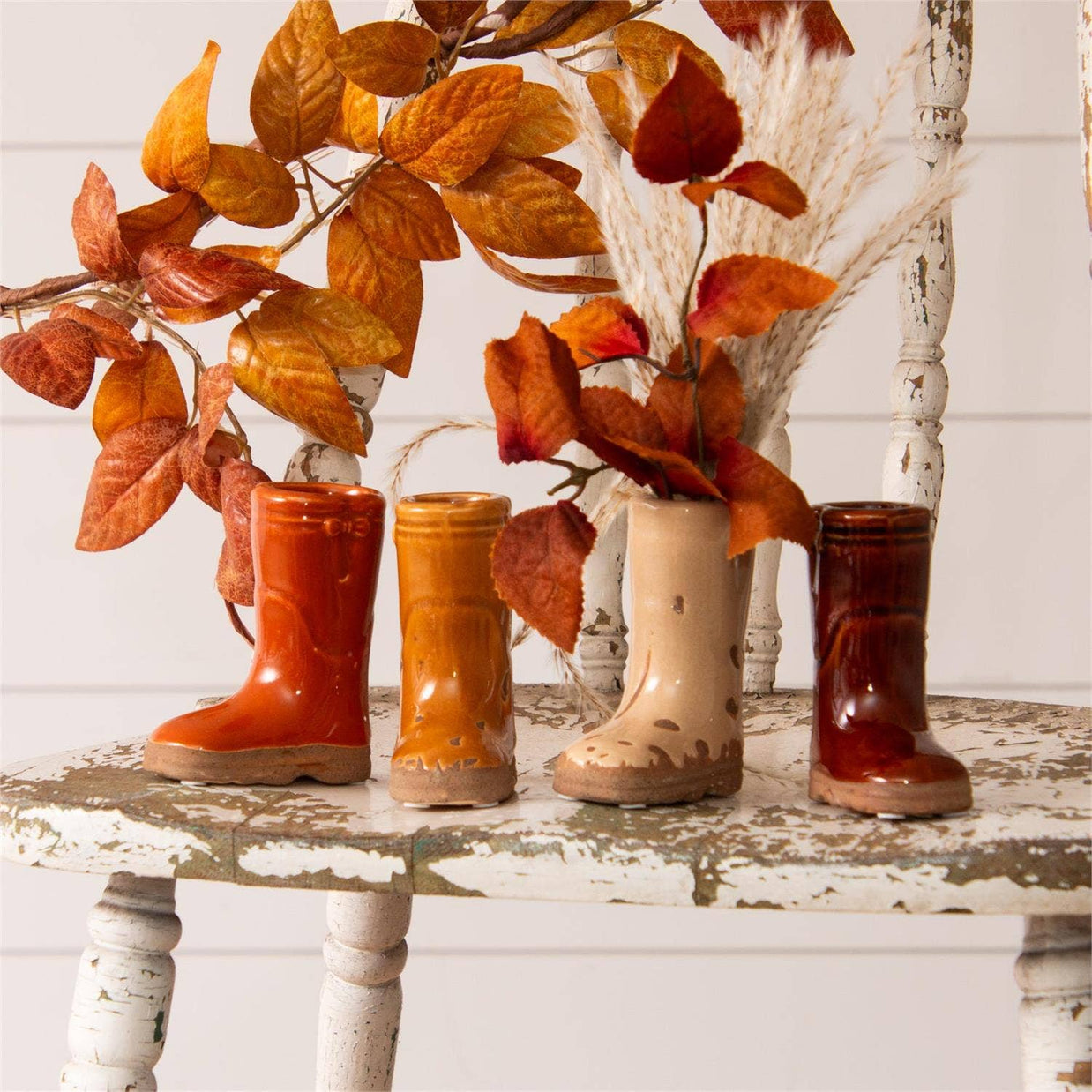 Four ceramic boots in different colors on a rustic wooden surface with autumn leaves.