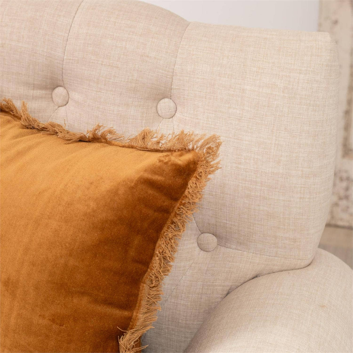 Beige armchair with a brown pillow featuring frayed edges.