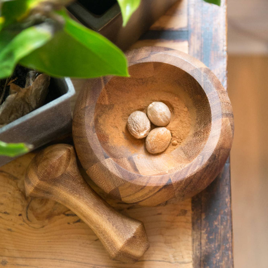 Wooden bowl with stones on a wooden surface with plants in the background