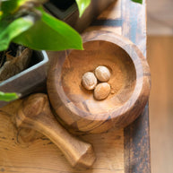 Wooden bowl with stones on a wooden surface with plants in the background