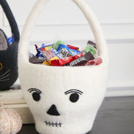 White skull-shaped basket with Halloween candy on a table.