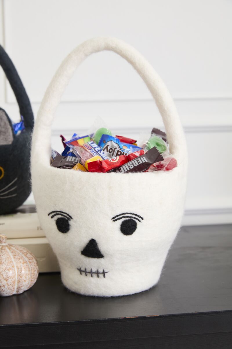 White skull-shaped basket with Halloween candy on a table.